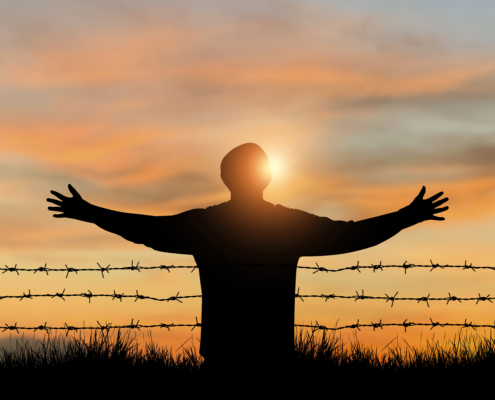 The young man stood alone with both arms raised on the top of the mountain in front of the barbed wire at sunrise. He felt a sense of freedom and a new beginning.